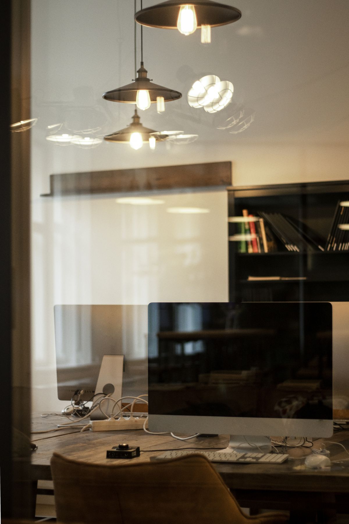 A warm home office desk with a large display, desk lamp and bookshelf