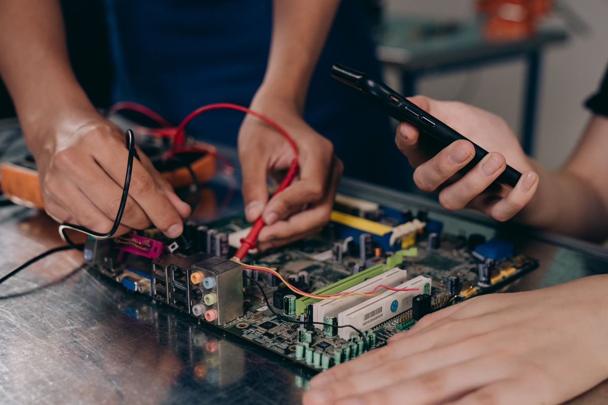Hands testing a circuit board with wires and a multimeter